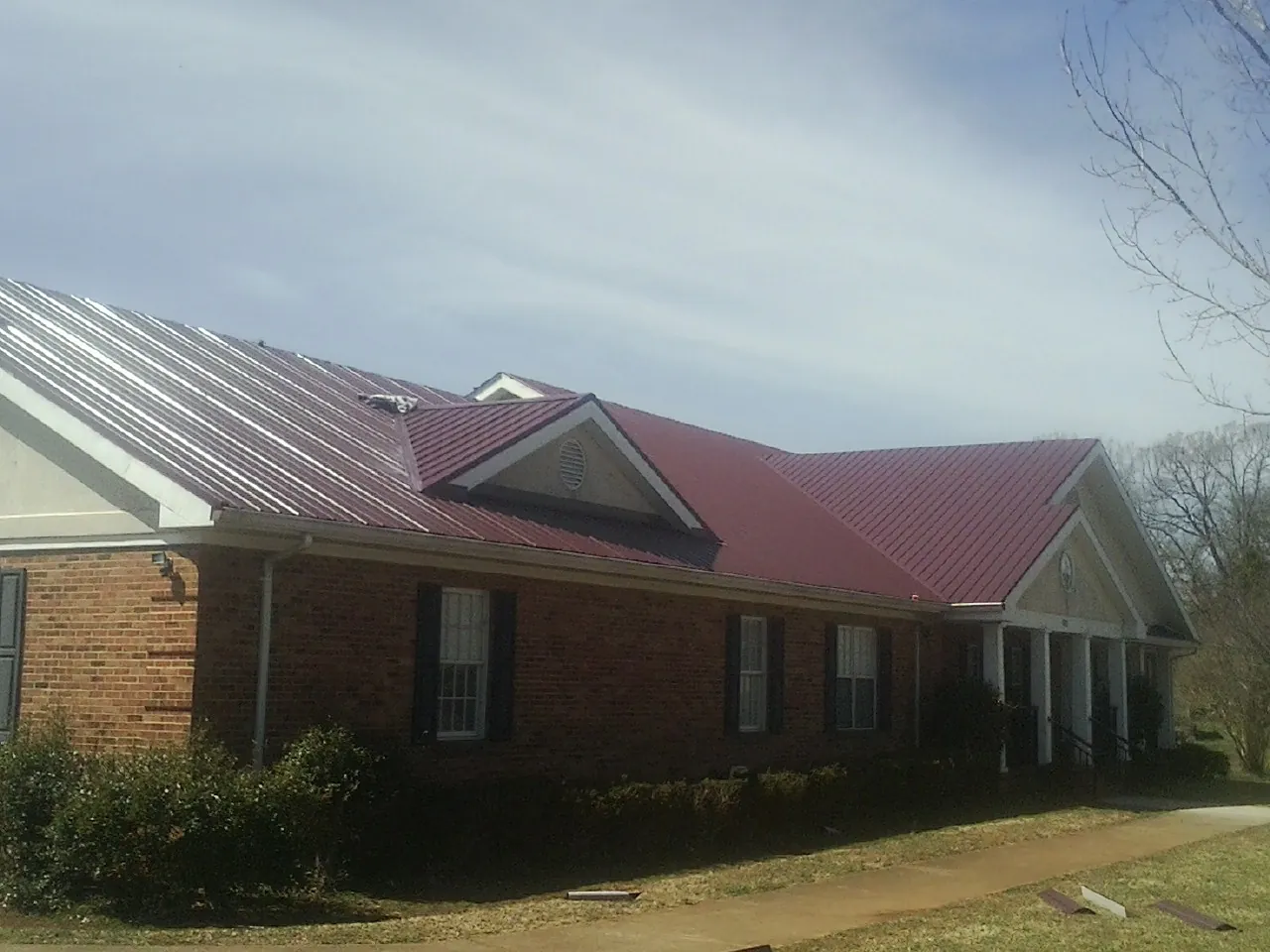 Red metal roof with gabled entries on a long brick building, from a Hail Damage Roof Repair job in Port Richey