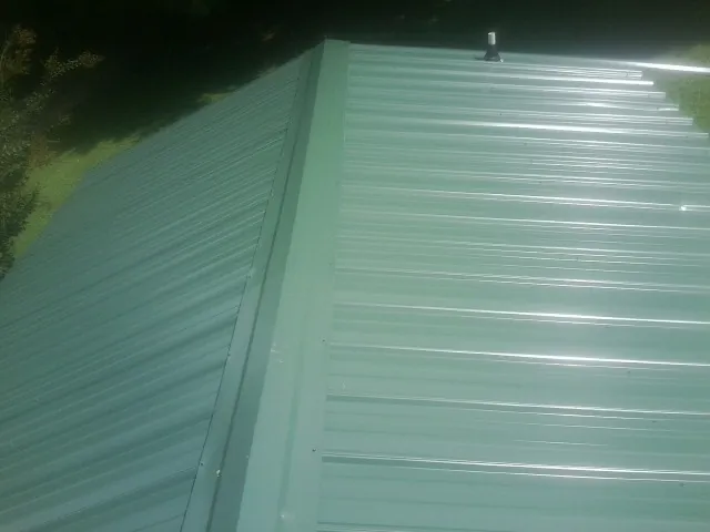 New green metal panels meeting at the ridge of a roof — Flat Roof Repair work by our crew in Port Richey