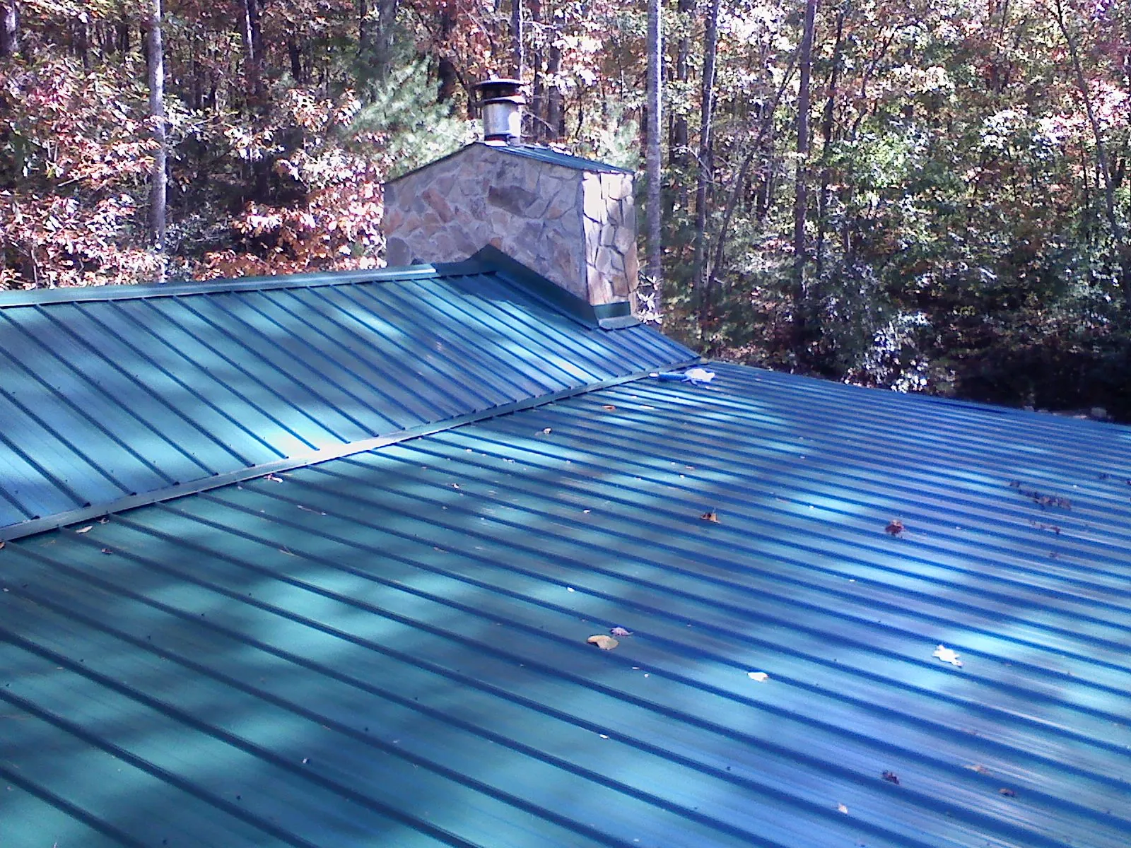 New green metal roof and stone chimney surrounded by autumn woods in Port Richey