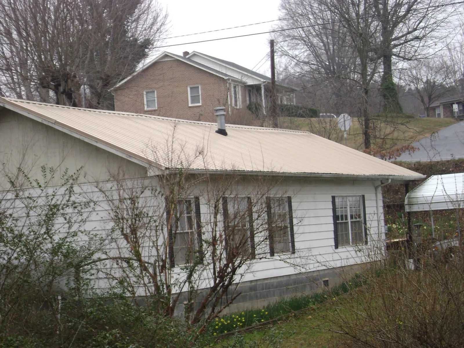 Tan metal roof on a white sided house set into a hillside — Commercial Roofing by Roofing Brothers in Port Richey
